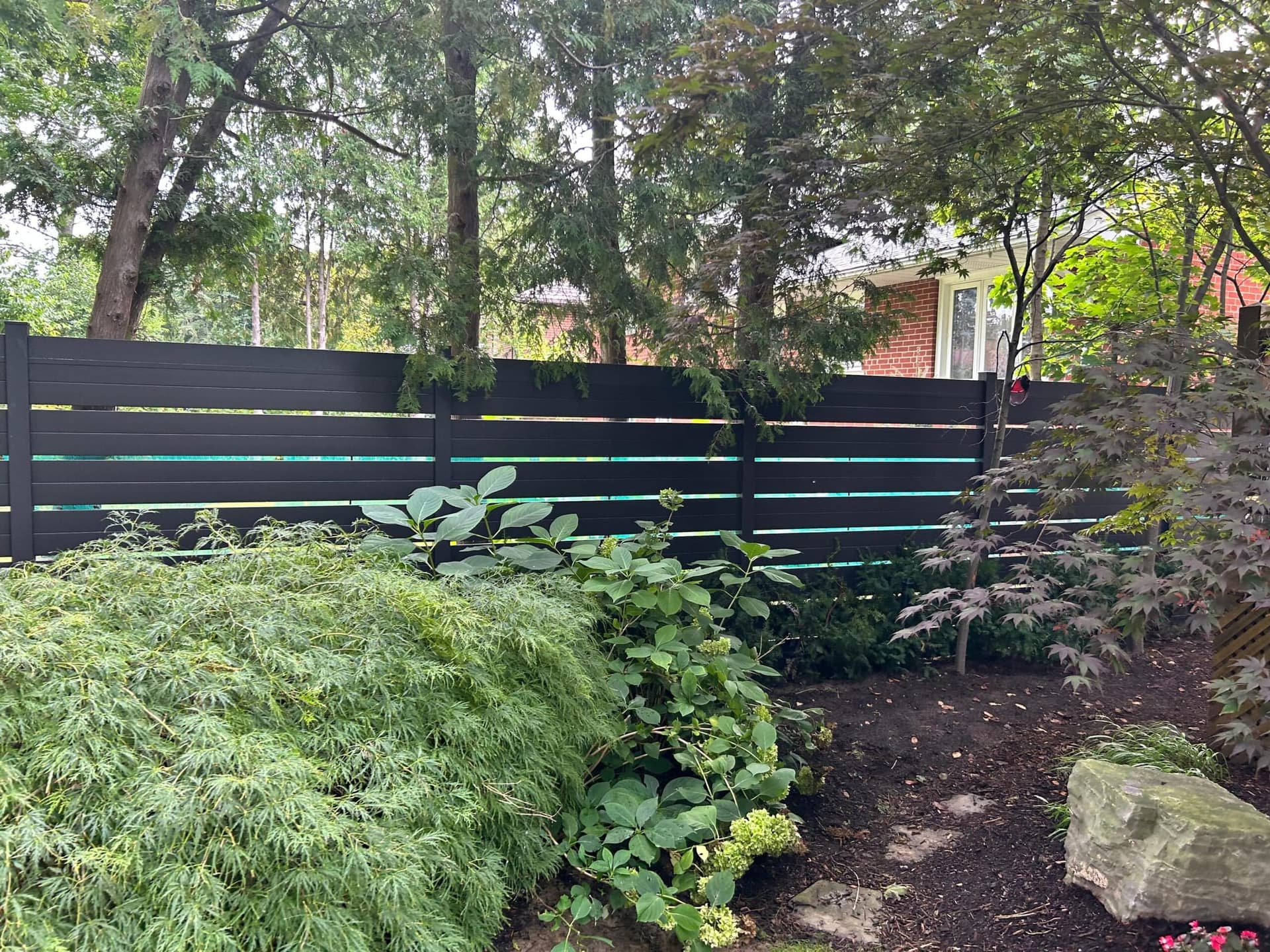 Black aluminum semi-privacy fence with spaced slats in a garden setting