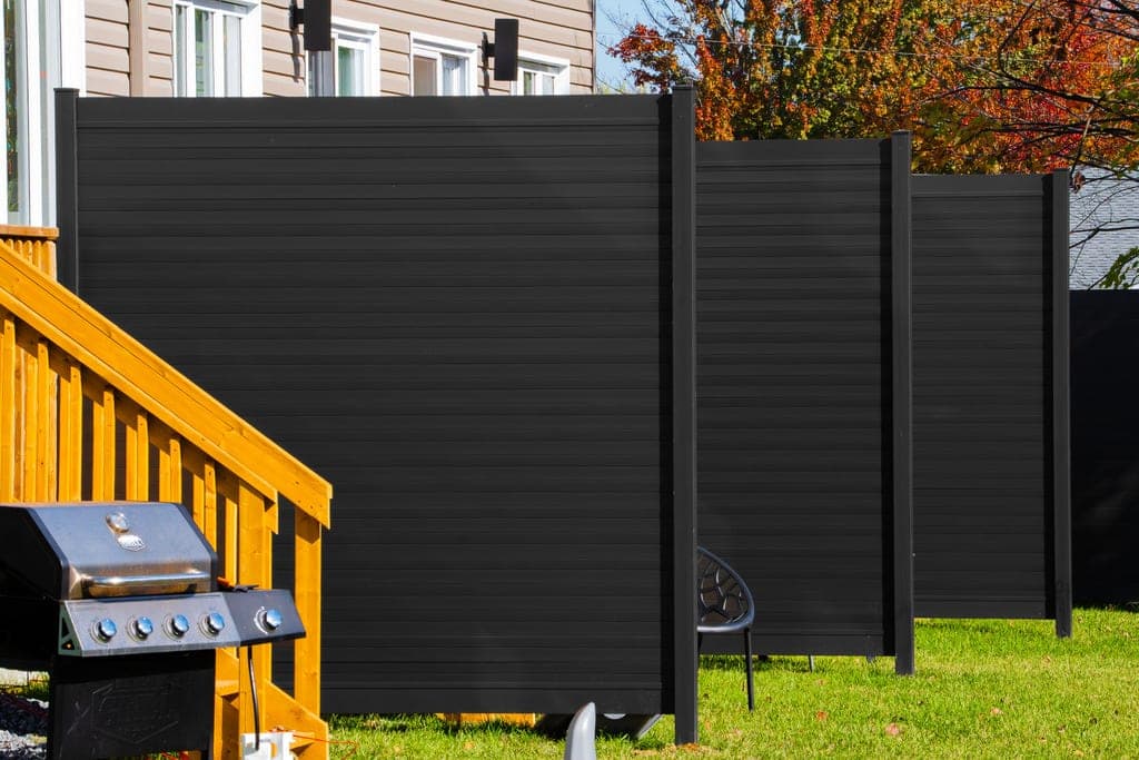 Black aluminum privacy fence in a residential backyard with a deck and gas grill