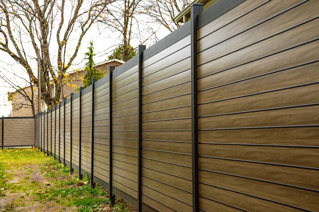 Long run of horizontal wood-grain aluminum privacy fence in a backyard with bare autumn trees