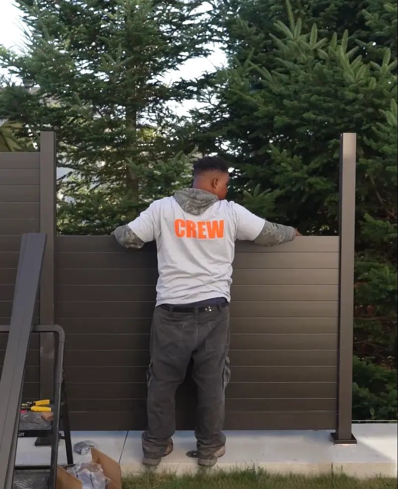 Installer securing an aluminum privacy fence panel to a post