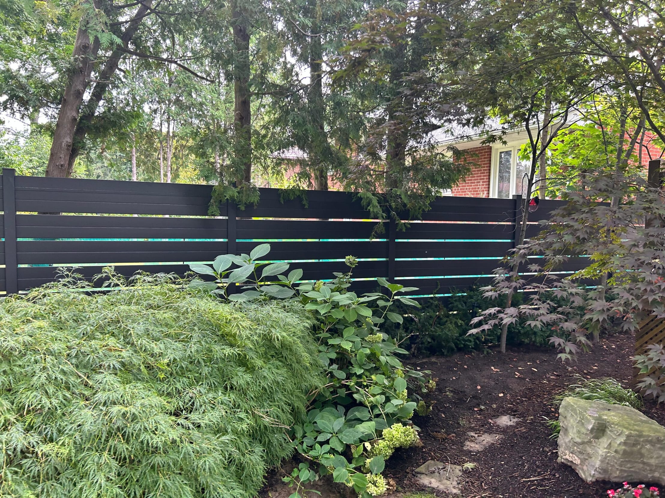 Black horizontal-slat aluminum fence panels installed along a landscaped garden bed