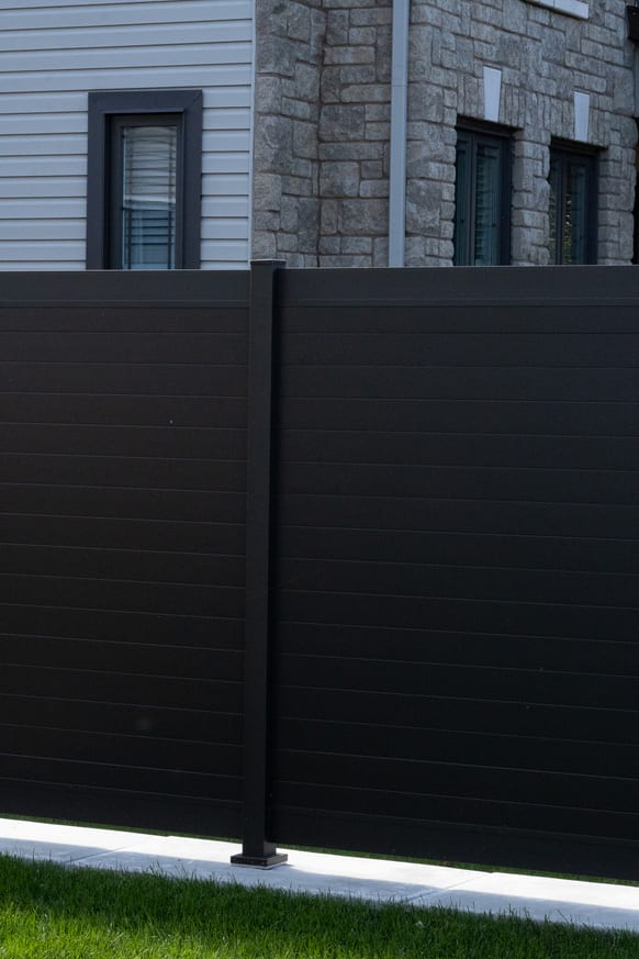 Aluminum fence post against a stone and siding house exterior